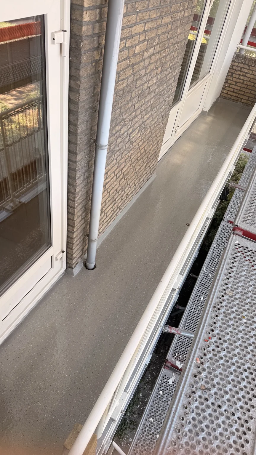 Grijze antislip balkonafwerking met deco chips naast witte deurkozijnen