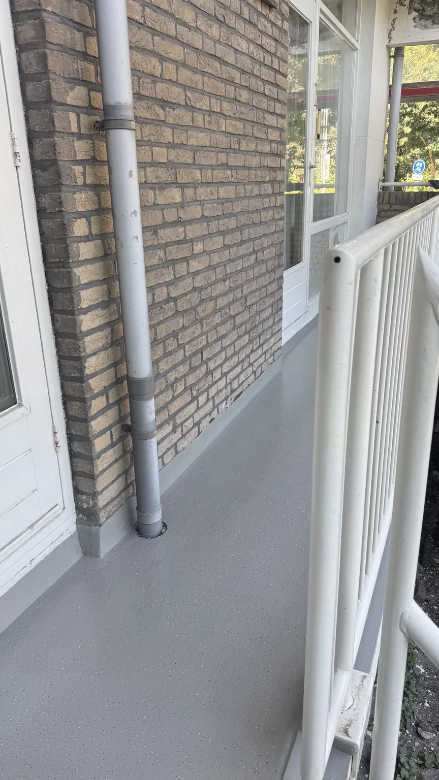 Balkonvloer met decoratieve chips en aansluitingen langs de gemetselde gevel